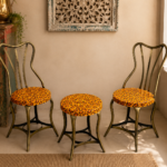 Bring warmth and character to your home with this handcrafted 3-piece bistro set featuring two vintage-inspired iron chairs and a matching round table. Finished in a cheerful antique yellow with intricate hand-painted floral artwork, this eye-catching set combines traditional craftsmanship with timeless elegance, making it perfect for balconies, patios, cafés, gardens, and indoor spaces. Specifications Set Includes: 2 Chairs + 1 Round Table Material: Iron Finish: Antique Yellow with Hand-Painted Floral Design Color: Antique Yellow Style: Vintage / Bohemian / Rustic / Cottage Suitable For: Balcony, Patio, Garden, Café, Bistro, Indoor Seating Condition: Vintage